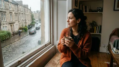 Mulher brasileira expatriada em apartamento na Europa olhando a rua pela janela, acolhendo a saudade, elaborando o luto migratório e reconstruindo sua identidade no exterior - Psicóloga Eliza Chagas.